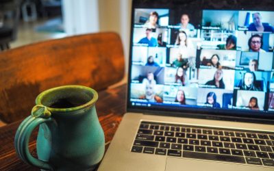 A laptop displaying a grid view of a virtual meeting with multiple participants on screen, alongside a turquoise ceramic mug on a wooden table.